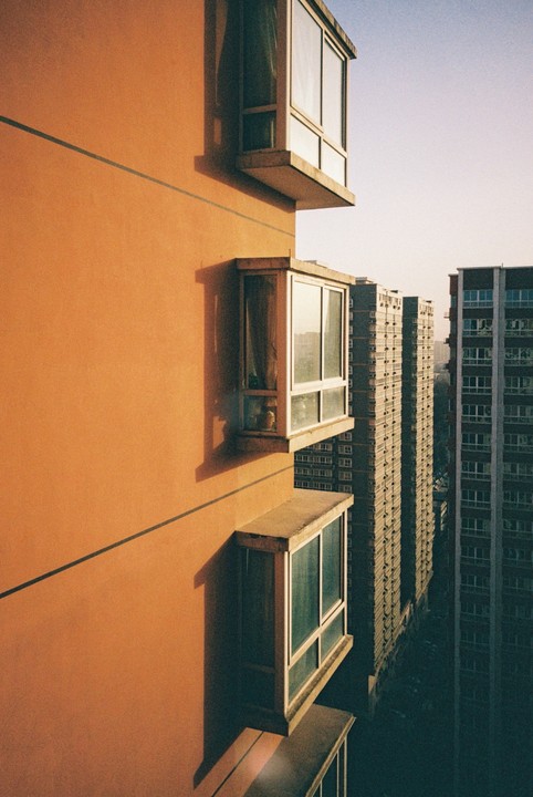 The side of a warm orange building with bay windows is shown next to other tall buildings.