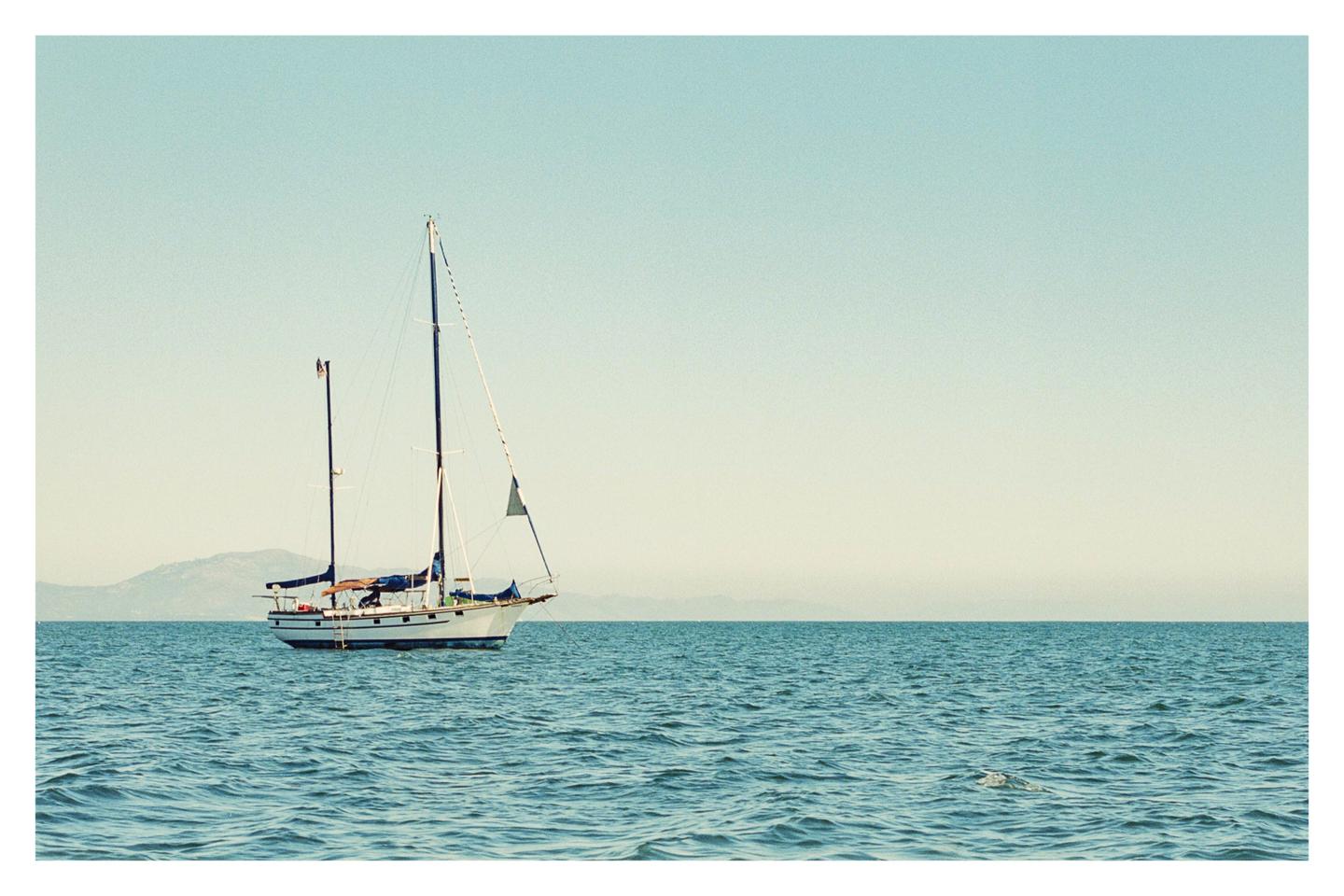 A sailboat floats on the water with mountains in the distance under a clear sky.