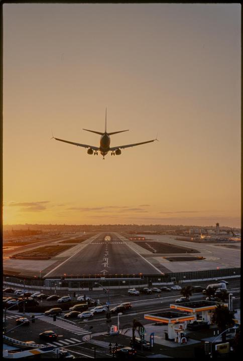A passenger airplane approaches a runway at sunset, with a street and gas station visible below.