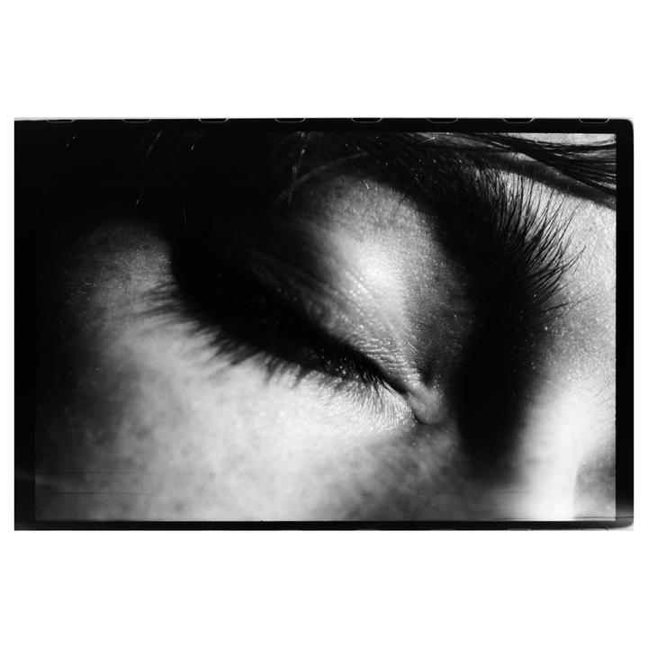 A close-up, black and white portrait shows a person's closed eye and eyelashes.