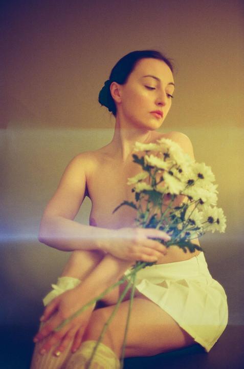 A woman with a bare torso and a white skirt sits holding a bouquet of white flowers.
