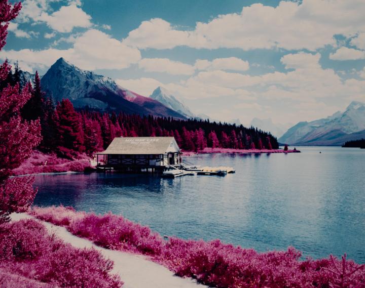 A boathouse sits on the shore of Maligne Lake, surrounded by mountains and trees.