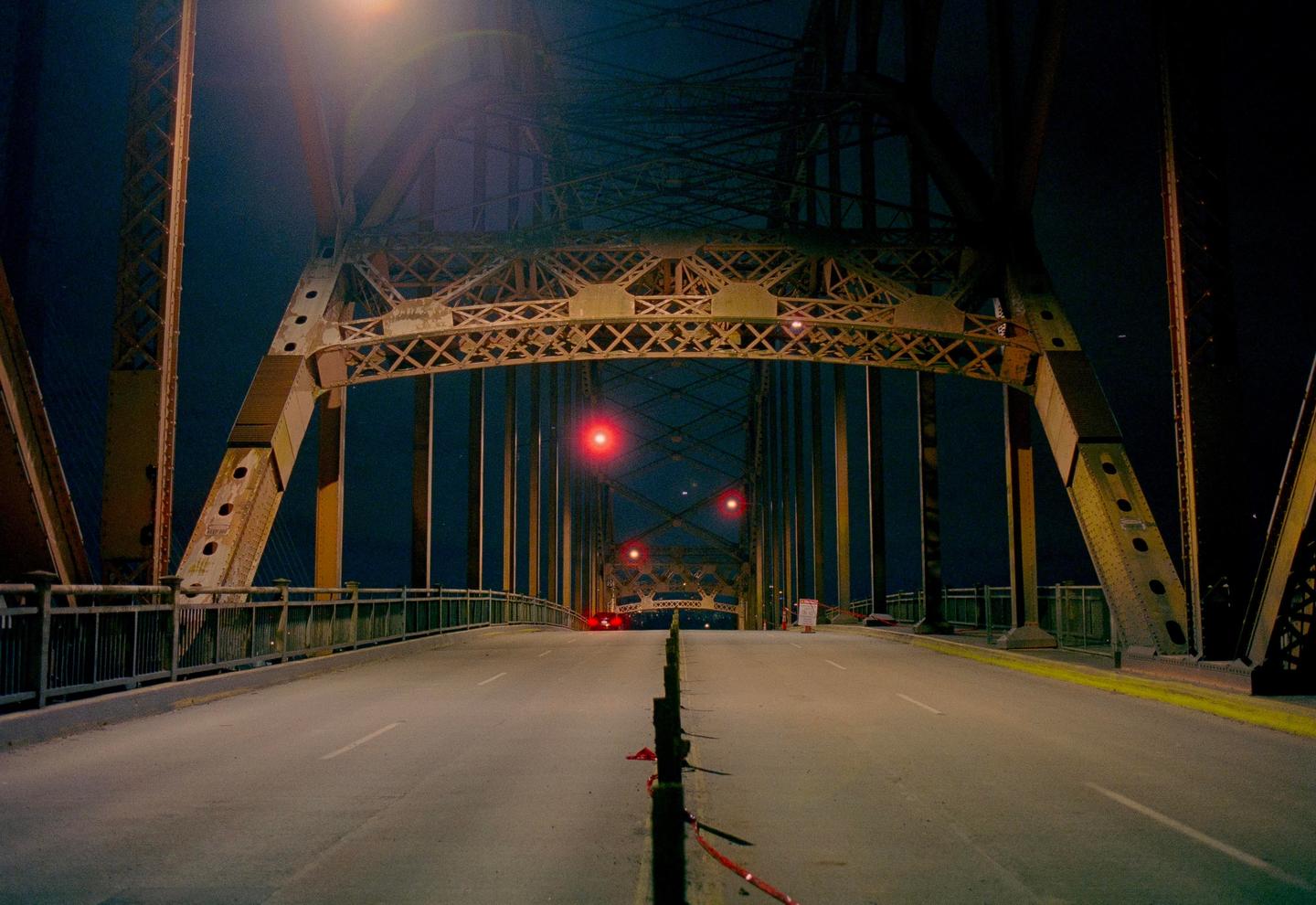 A long exposure shows a bridge at night with red lights in the distance.