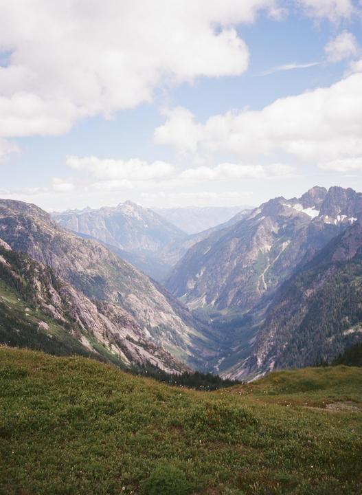 A valley with a river running through it is surrounded by mountains under a cloudy sky.