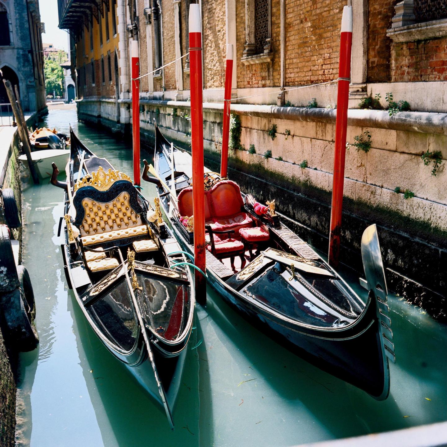 Two gondolas are moored in a canal next to a brick building.
