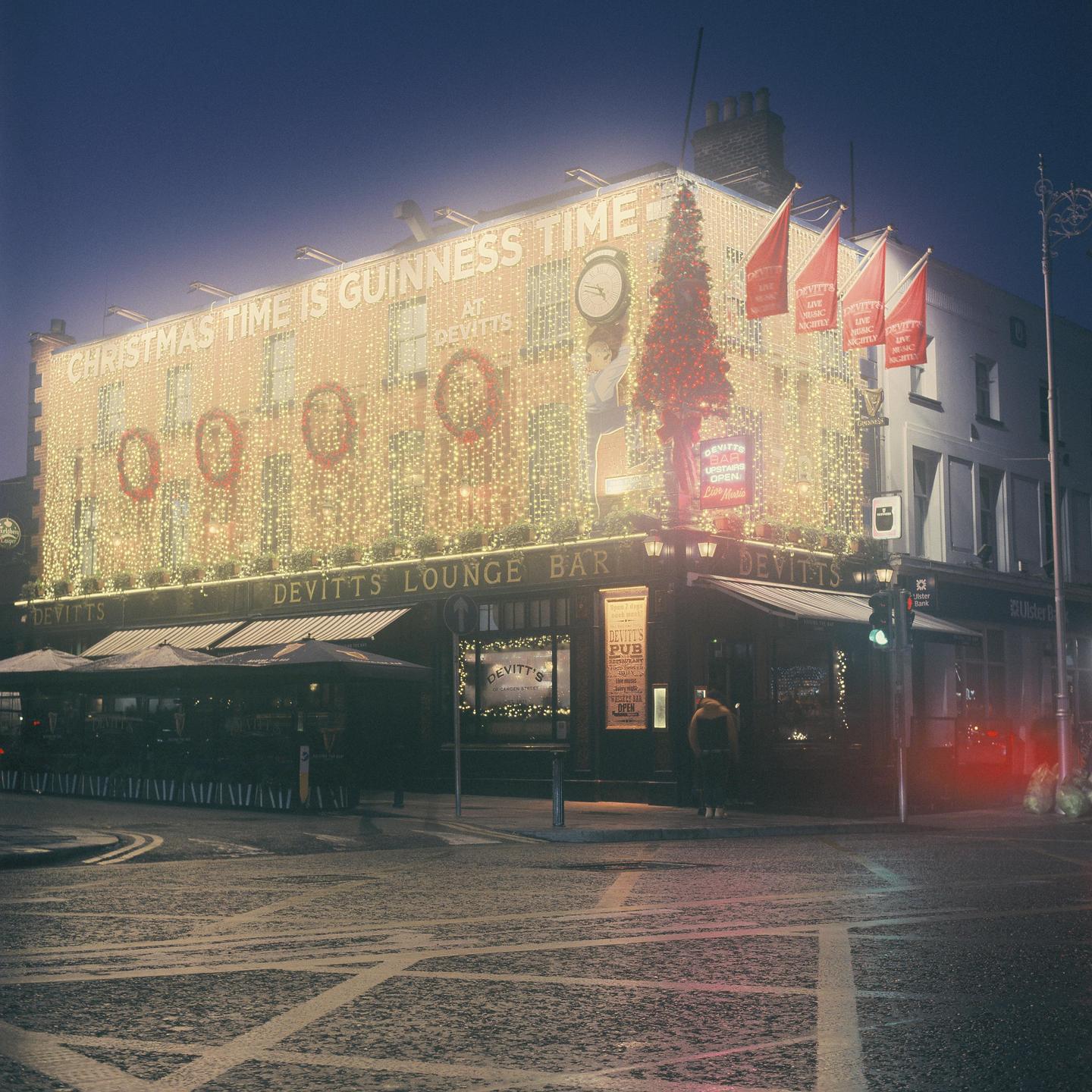 A building with Christmas lights and decorations is illuminated at night, with a street and crosswalk in the foreground.