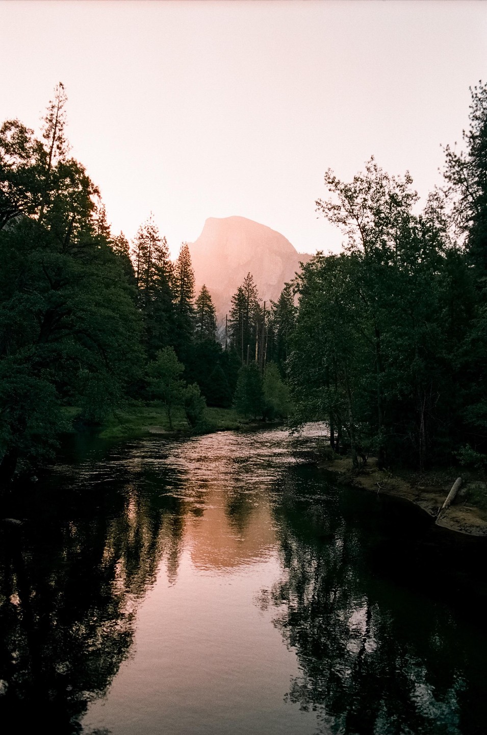 A river flows through a forest with a mountain in the background at sunrise.