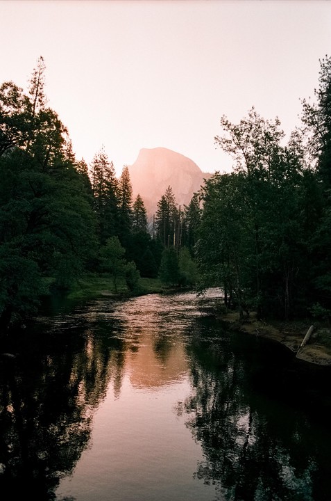 A river flows through a forest with a mountain in the background at sunrise.