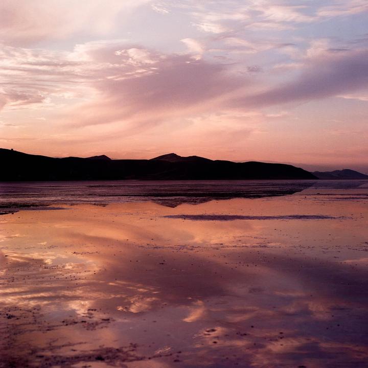 A body of water reflects the pink and purple sky at sunset with mountains in the distance.