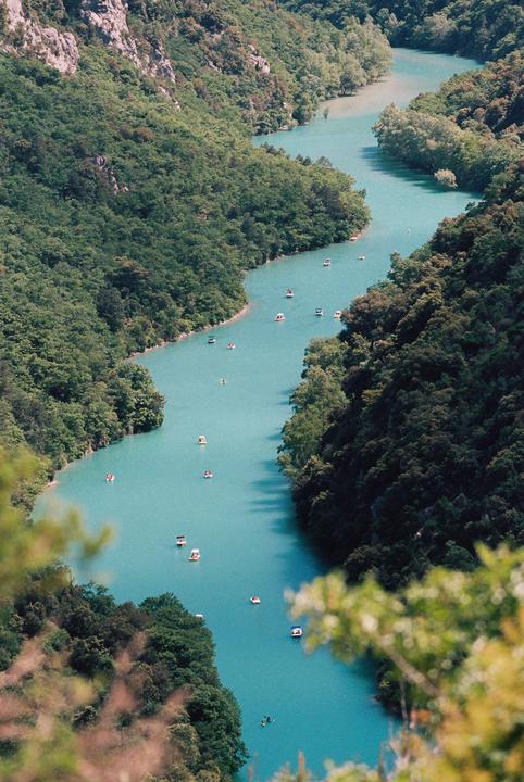 A winding turquoise river with many small boats is surrounded by lush green mountains.
