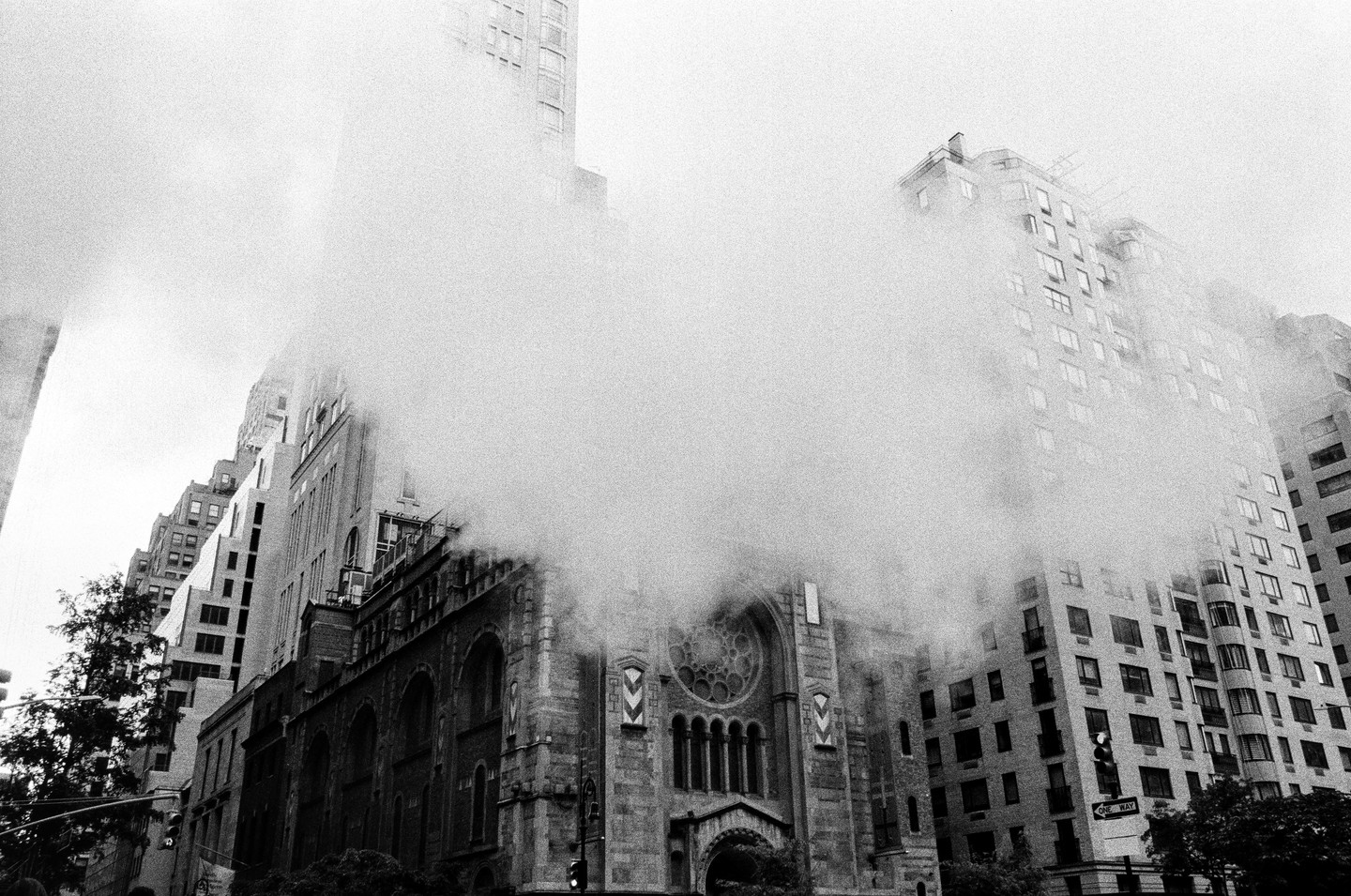 Steam billows from a street in front of a church and tall buildings in a city.