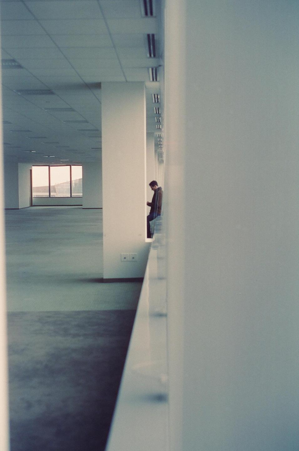 A man stands in a large, empty room with a window looking out onto a landscape.
