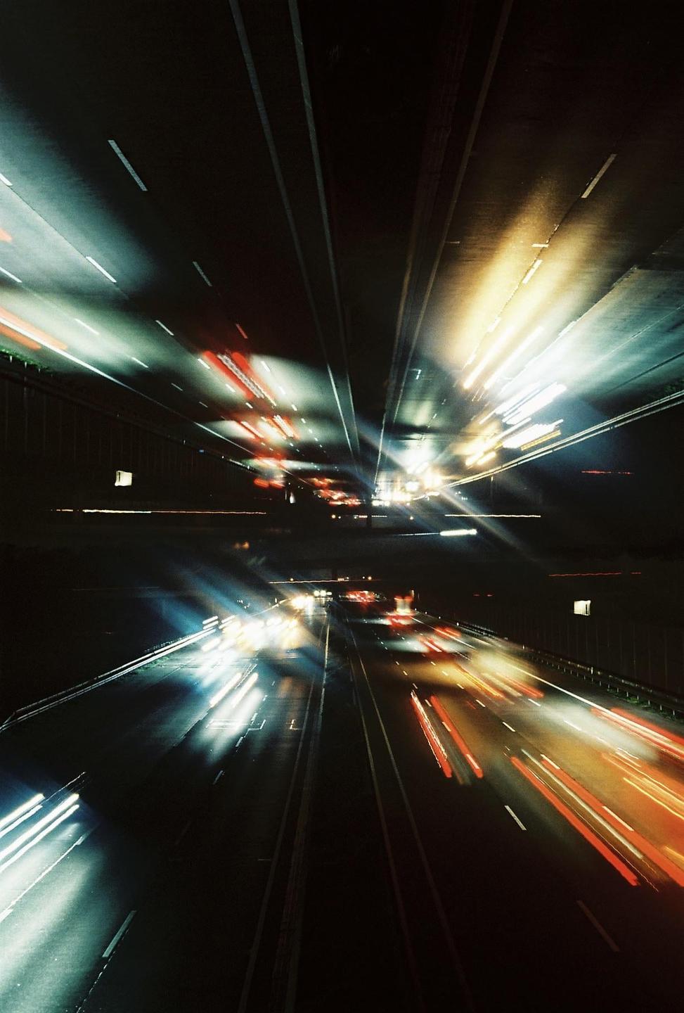 Light trails from vehicles on a highway at night are reflected in a mirror image.