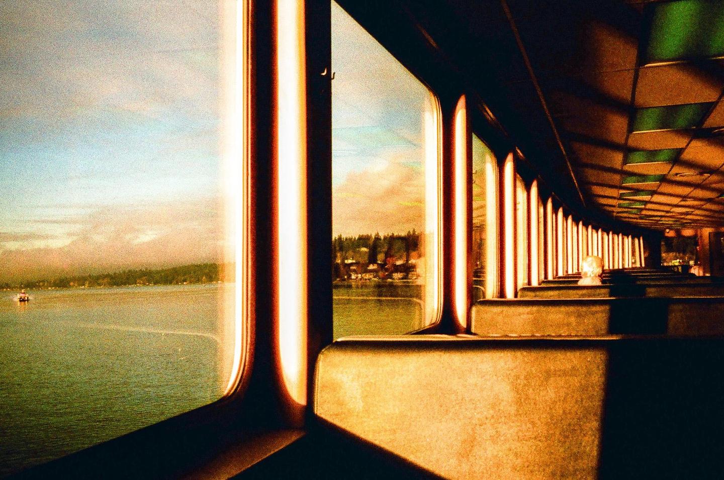 The interior of a ferry with rows of seats and windows looking out onto a body of water and distant land.