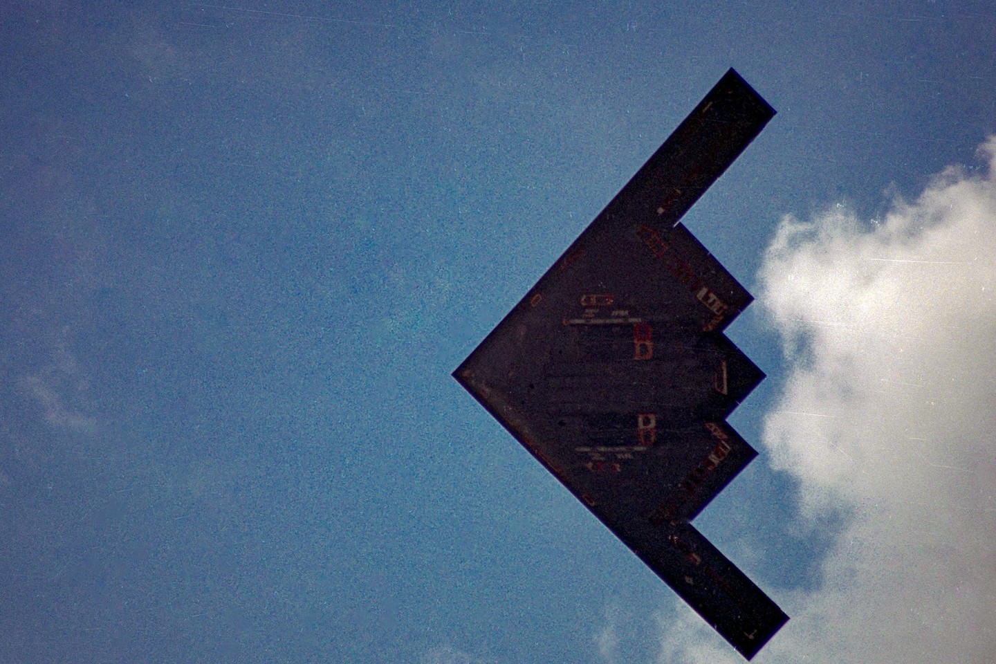 A B2 bomber flies through a blue sky with white clouds.