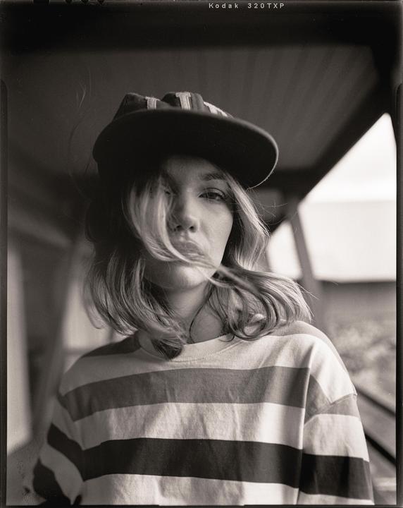 A woman wearing a striped shirt and a baseball cap looks directly at the viewer.