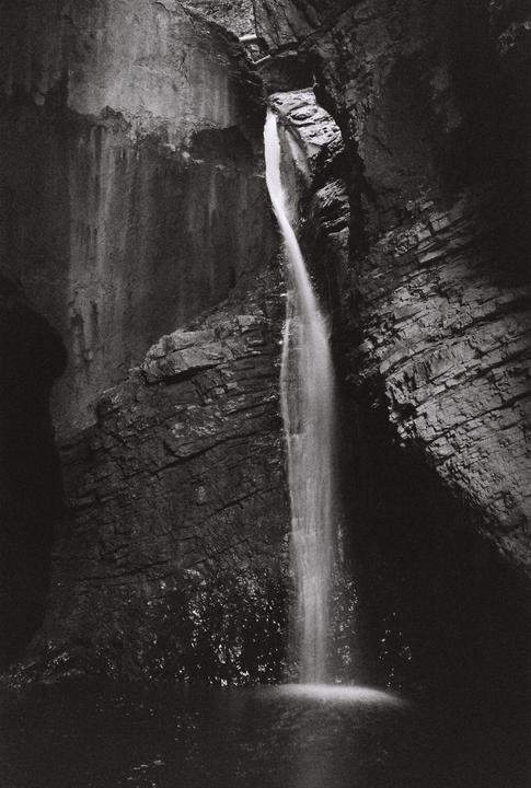 A waterfall cascades into a pool surrounded by dark, rocky cliffs.
