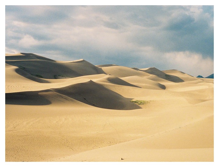 A vast desert landscape features numerous sand dunes under a cloudy sky.
