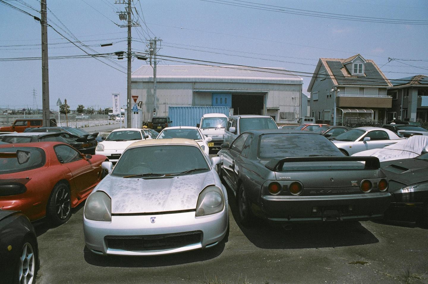 A parking lot full of cars is visible in front of a building and a house.