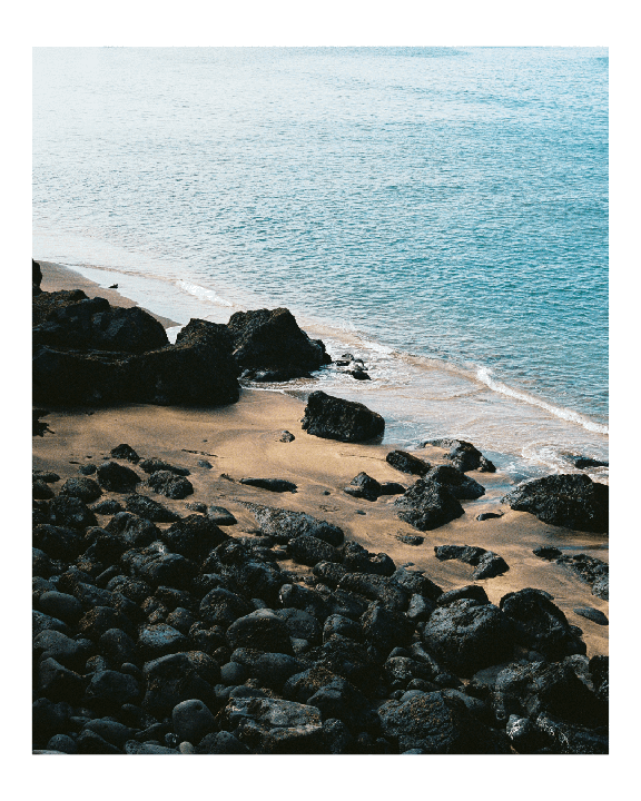 Waves wash onto a sandy beach covered with dark volcanic rocks.