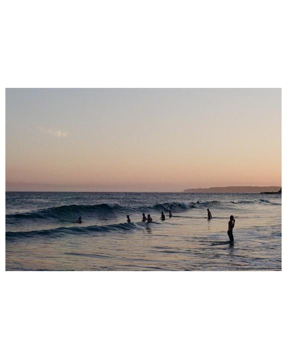 A group of people are swimming in the ocean at sunset.