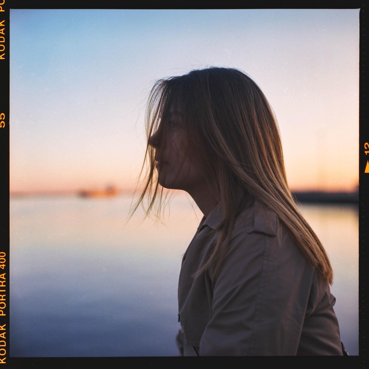 A woman with long hair looks out over the water at sunset.