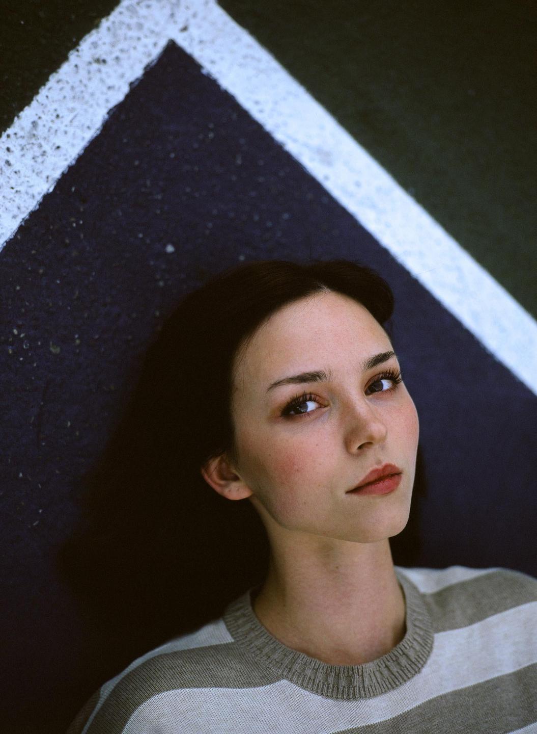 A woman with dark hair and a striped sweater lies on a surface with painted lines.