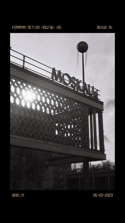 The sun shines through a patterned wall of a building with the word "MOSKAU" on its roof.