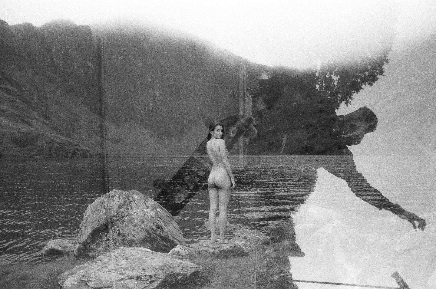 A double exposure shows a nude woman standing on rocks by a lake, superimposed with a man reaching into water and a tree.