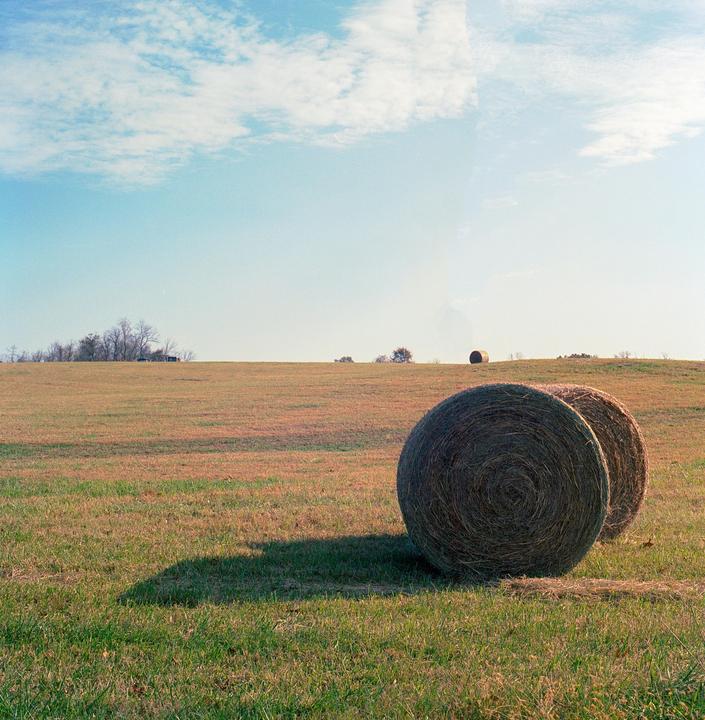 Two large hay bales sit in a field under a blue sky with scattered clouds.