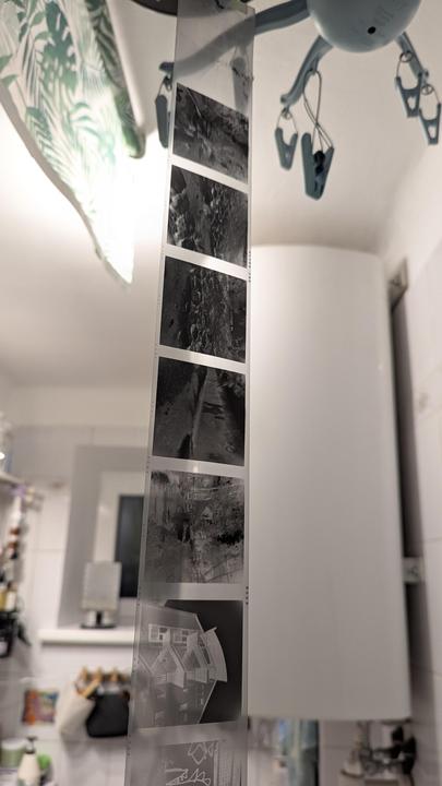 A strip of black and white film hangs vertically, displaying several negative images, in a room with white walls and a patterned curtain.