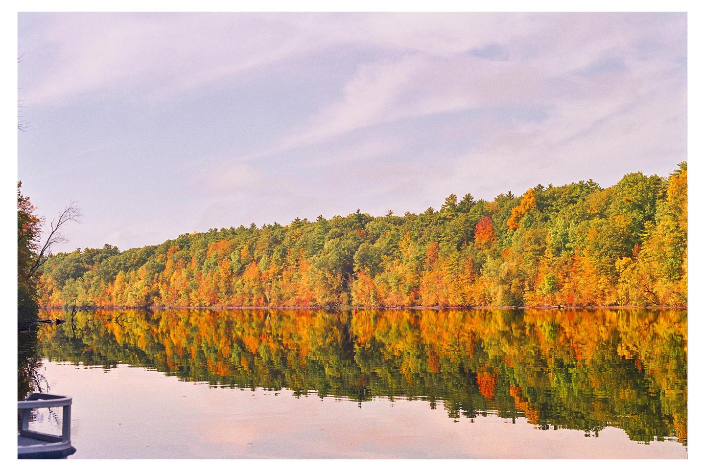 A colorful autumn forest is reflected in the still water of the Hudson River.