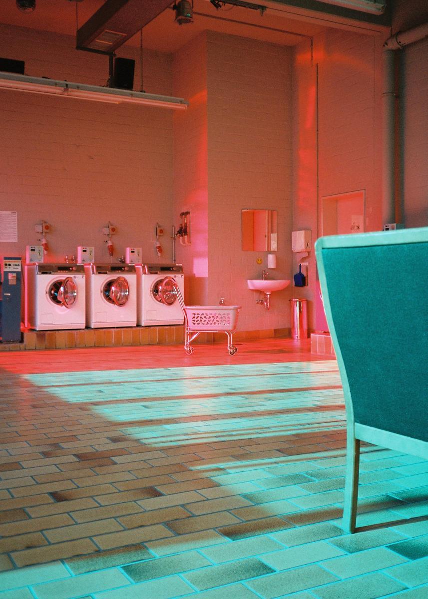 A laundromat with several washing machines and a sink is illuminated by red and blue light.