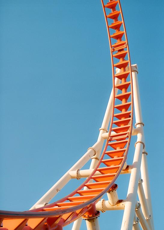 An orange roller coaster track curves upwards against a clear blue sky.