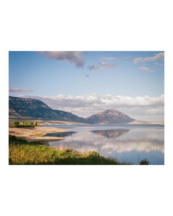 A calm lake reflects mountains and a cloudy sky.