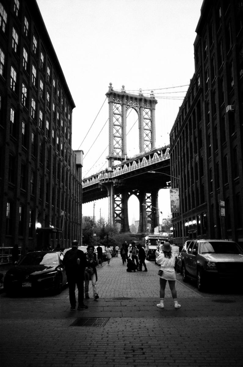 A street in New York is framed by buildings on either side, with the Manhattan Bridge visible in the distance.