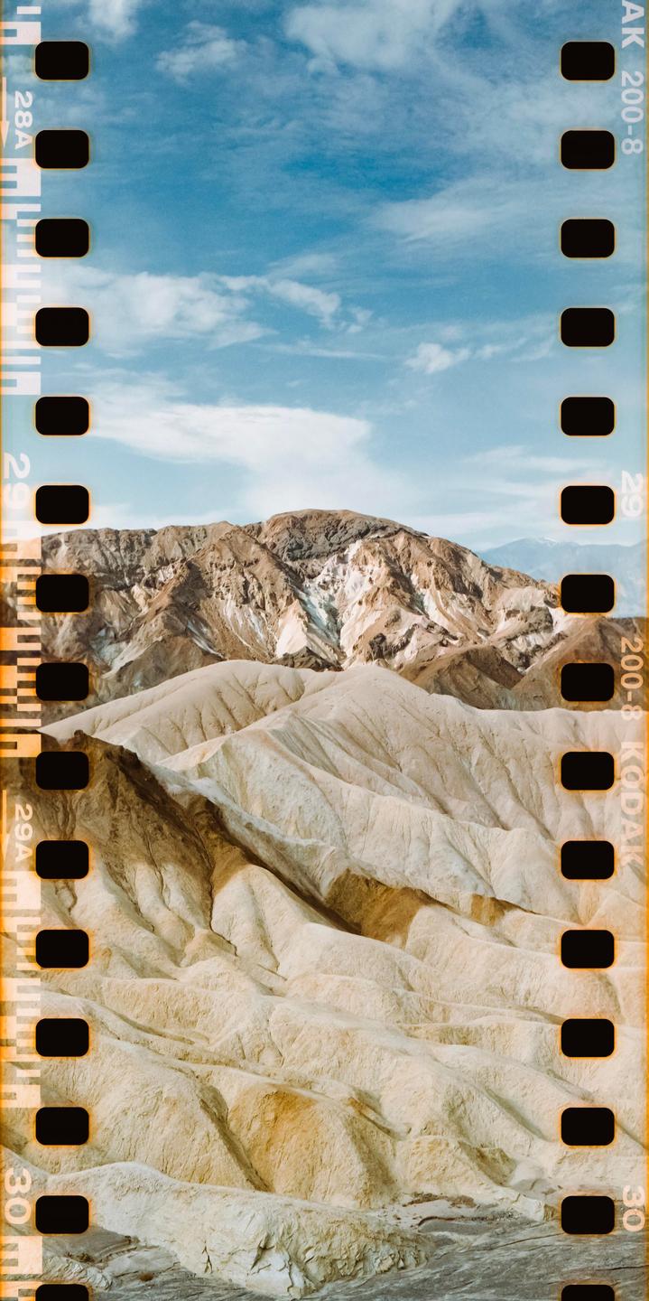 A desert landscape shows rolling hills and mountains under a blue sky with scattered clouds.