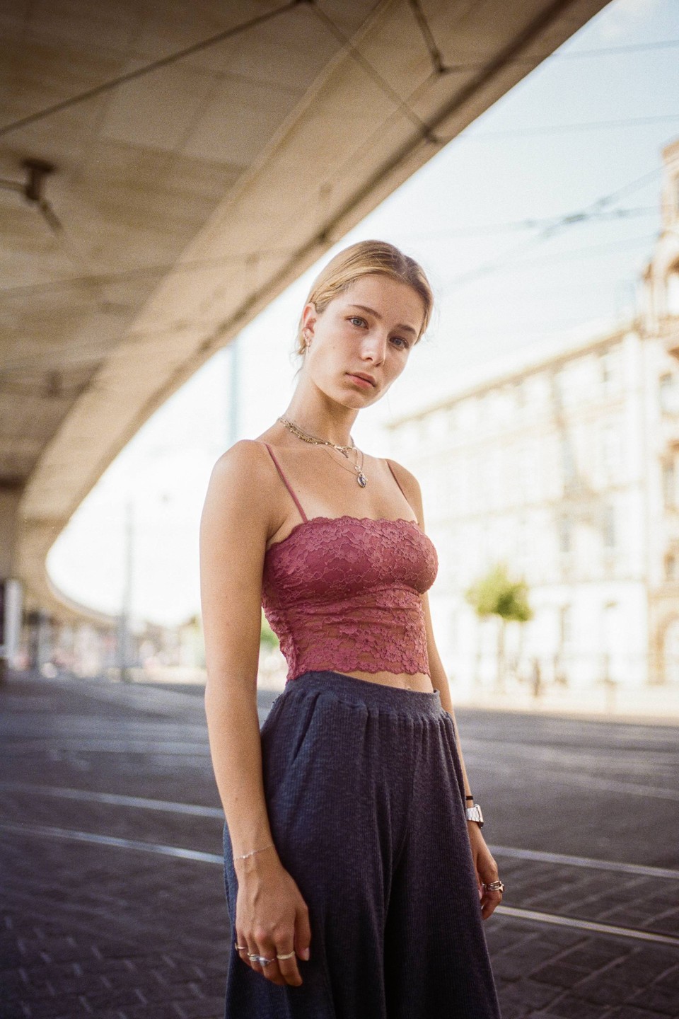 A woman stands on a street with an overpass above her.
