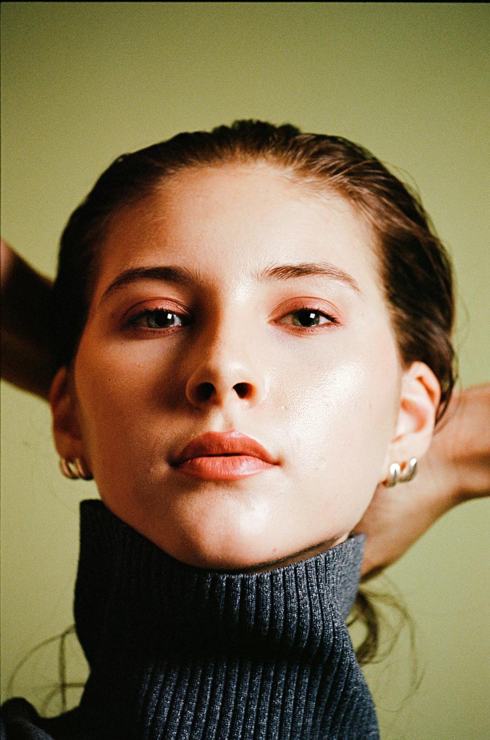 A woman with wet hair and a turtleneck sweater looks directly at the viewer.