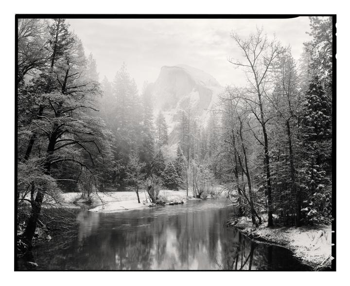 A river flows through a snow-covered forest with a large mountain in the background.