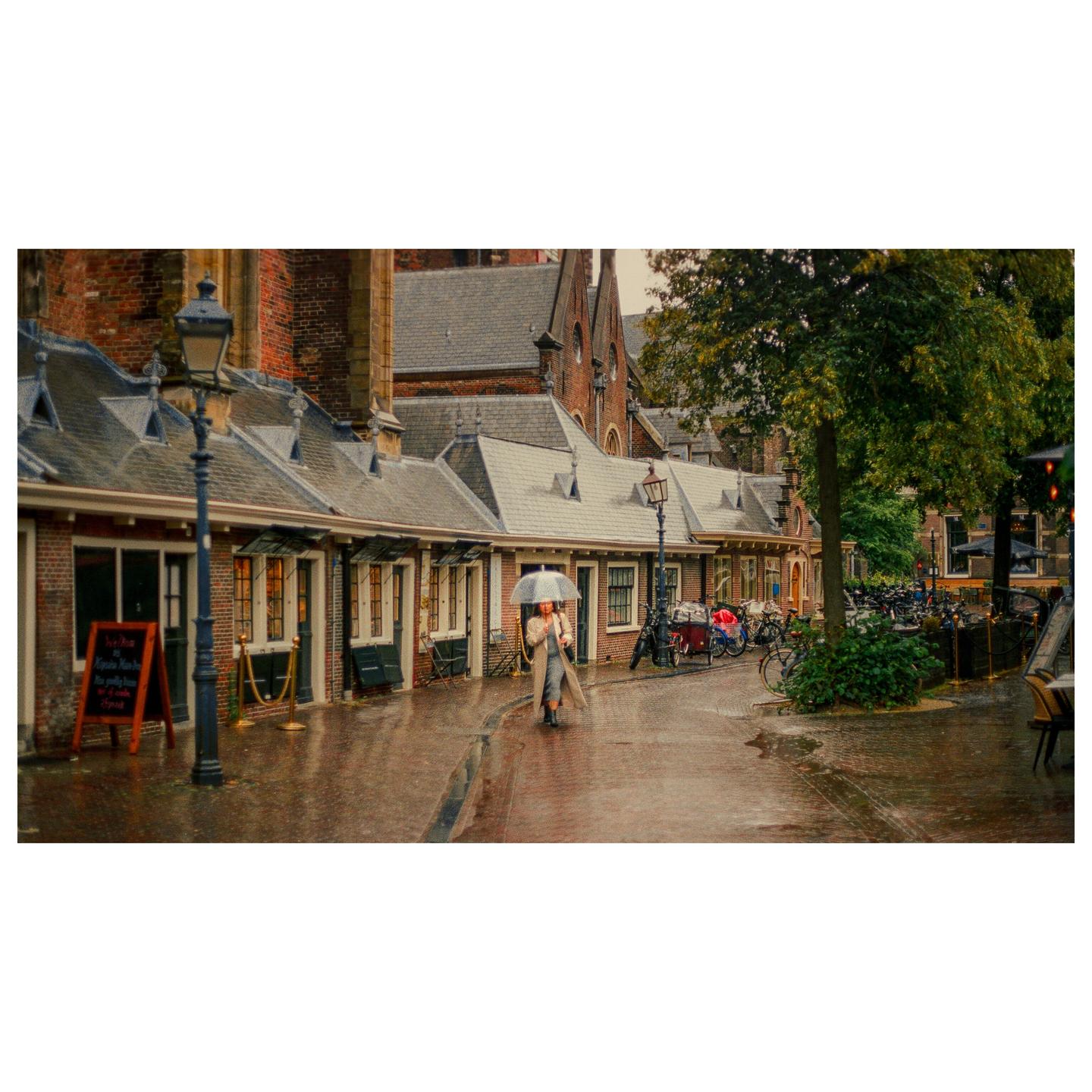 A woman with an umbrella walks down a wet street lined with brick buildings and bicycles.