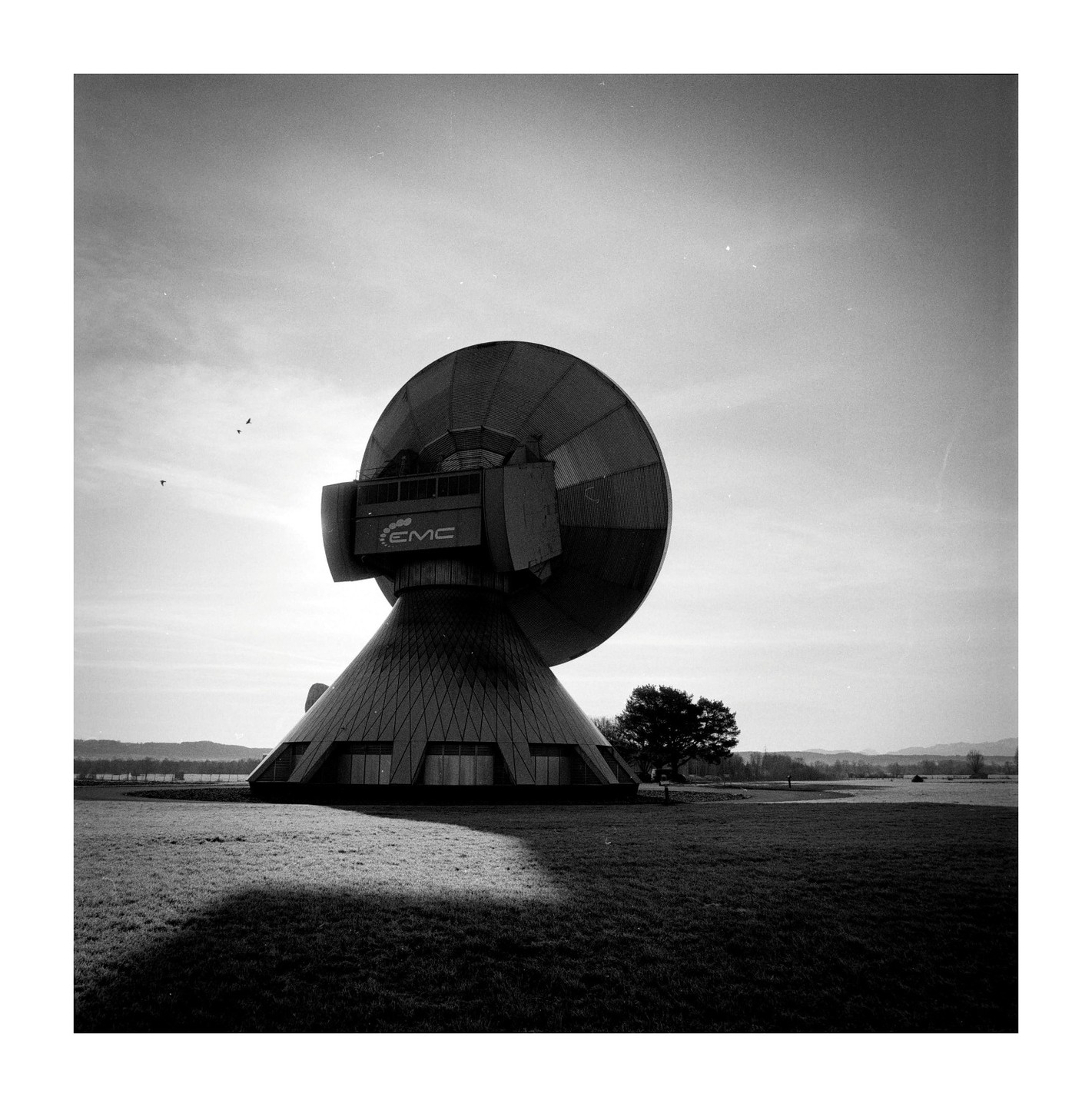 A large satellite dish stands in a grassy field under a bright sky.