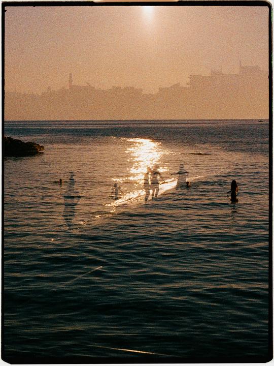 A double exposure shows people in the water with a city skyline in the background.