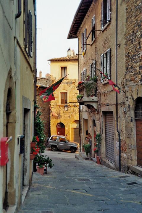 A narrow street in an old town is lined with stone buildings and a small car is parked at the end of the street.