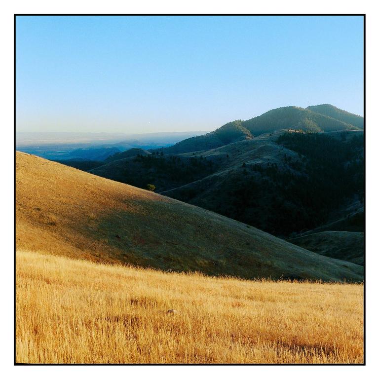 A landscape view shows rolling hills covered in golden grass and distant mountains under a clear sky.