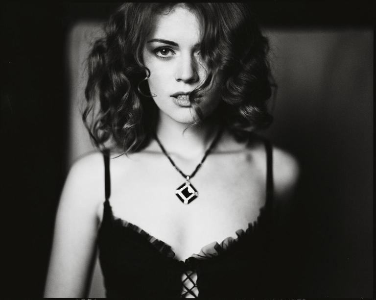 A woman with curly hair and a necklace looks directly at the viewer.