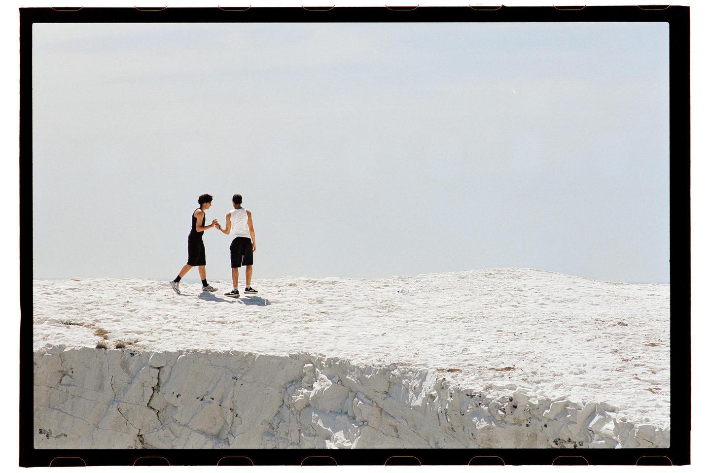 Two men stand on a white cliff overlooking a vast expanse of sky.