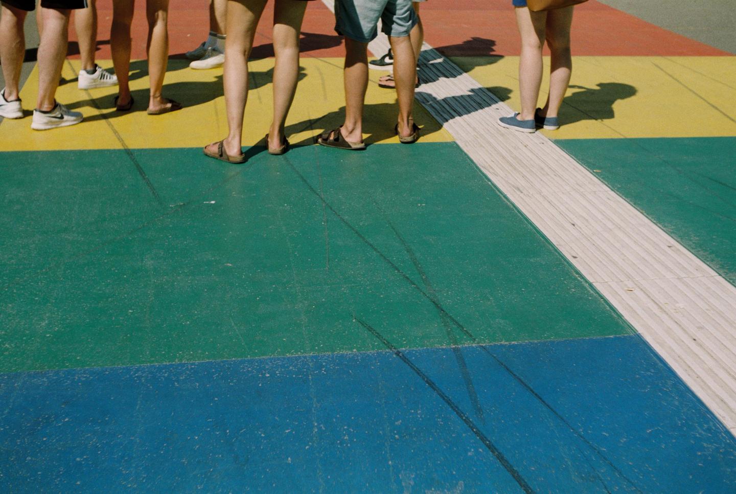 Several people stand on a colorful ground with shadows cast behind them.