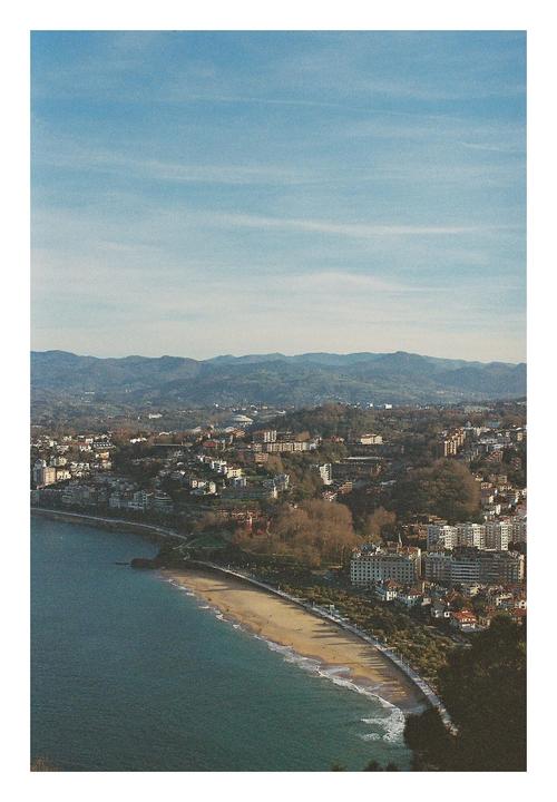 A city with a beach and mountains in the background is visible from an elevated perspective.