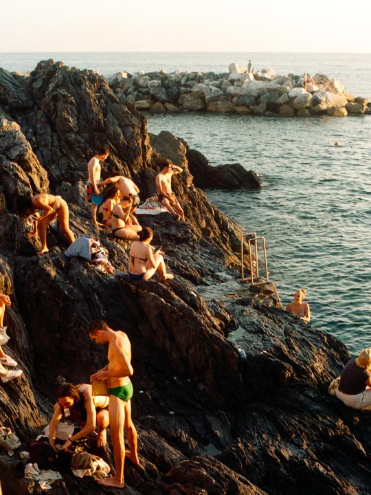 People are relaxing on a rocky shore next to the ocean.